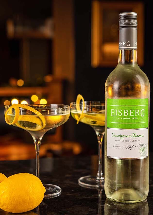 Two Elderflower Martini Mocktails garnished with lemon peels next to a bottle of Eisberg Sauvignon Blanc