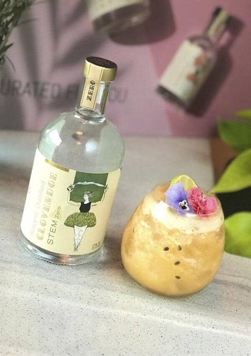 Lychee Passionfruit Caprioska garnished with edible flowers next to a bottle of Clovendoe Stem
