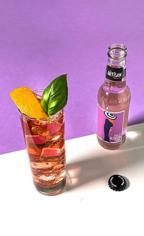Bottle of Artisan Drinks Violet Blossom Tonic next to a bold spritz mocktail drink