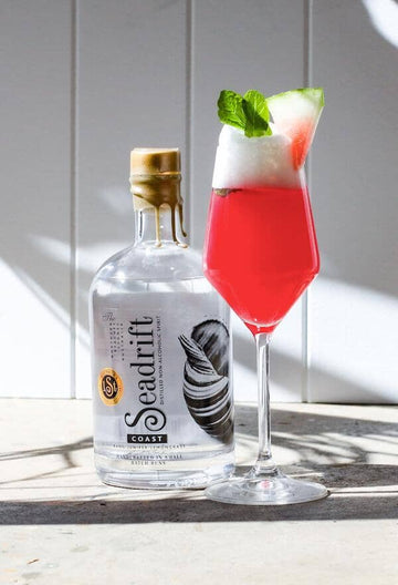 Watermelon gin mocktail farnished with mint leaves and a slice of watermelon next to a bottle of Seadrift coast