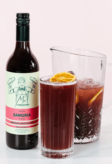 Bottle of Mr Consistent Sangria next to a glass and jug of sangria mocktails garnished with orange slices
