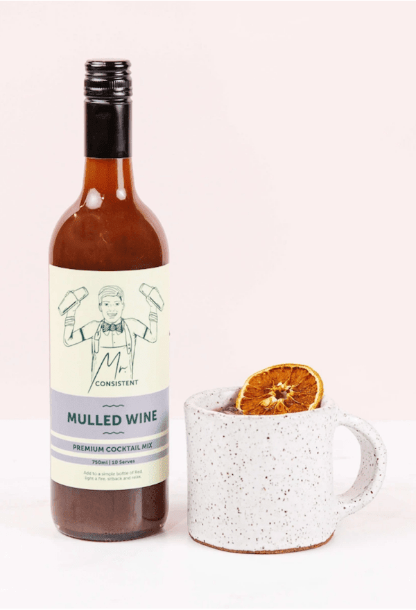 Bottle of Mr. Consistent Mulled Wine mix next to a mug of mulled non-alcoholic wine garnished with orange slices