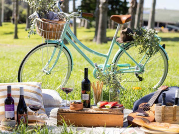 A picnic set up with three bottles of non-alcoholic wine and a bike 