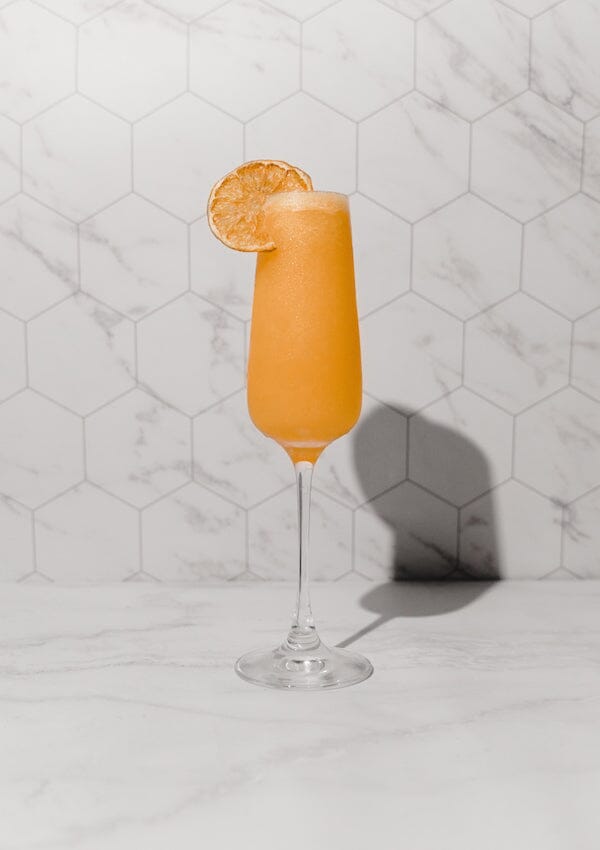 Classic mimosa mocktail garnished with a wheel of dried orange in a champagne glass