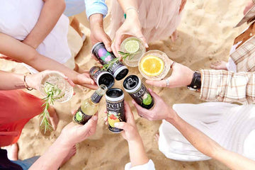 Eight hands holding ETCH non-alcoholic drinks cans and mocktails at the beach Sans Drinks