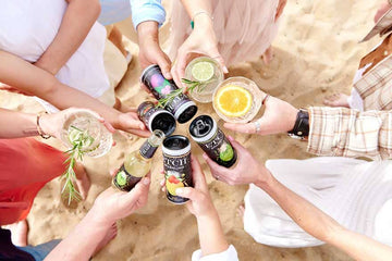 Eight hands holding ETCH non-alcoholic drinks cans and mocktails at the beach
