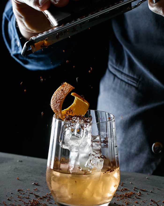 Person garnishing an Old Fashioned Whiskey mocktail with grated chocolate