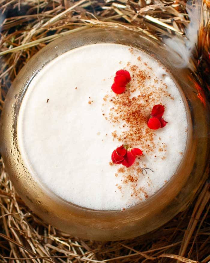 Round glass cup of creamy non-alcoholic rum mocktail garnished with cinnamon and edible flower petals