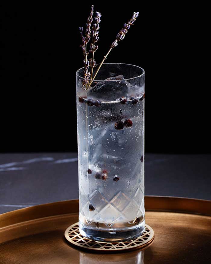 Gin and tonic mocktail in a tall glass garnished with twigs lavender and juniper berries