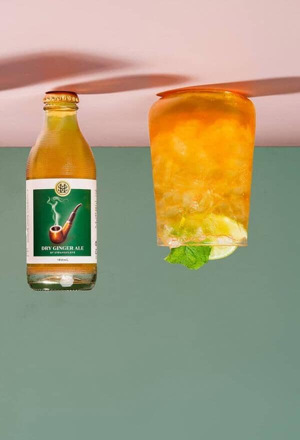 Ginger Spice Mocktail garnished with mint leaves next to a bottle of StrangeLove Dry Ginger Ale