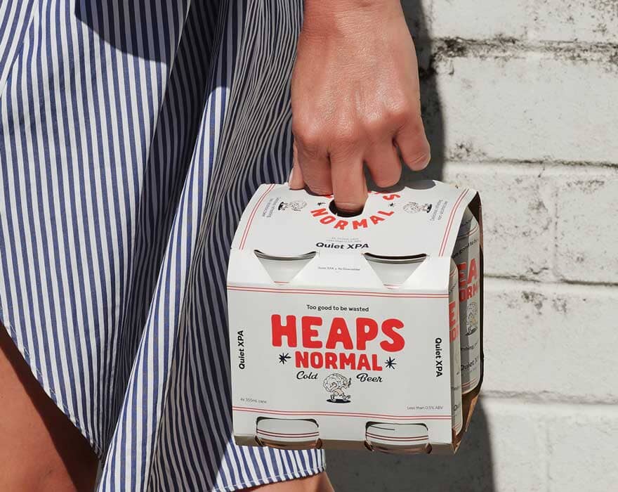 A woman holding a four pack of heaps normal non-alcoholic beer