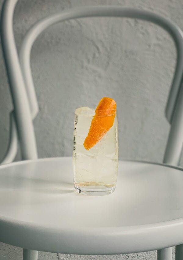 Gin mocktail garnished with an orange peel placed in a white chair