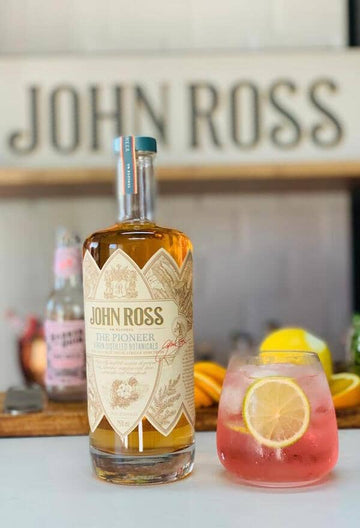 Gin Mocktail in a glass filled with ice garnished with lime wheels next to a bottle of JR The Pioneer Sans Drinks