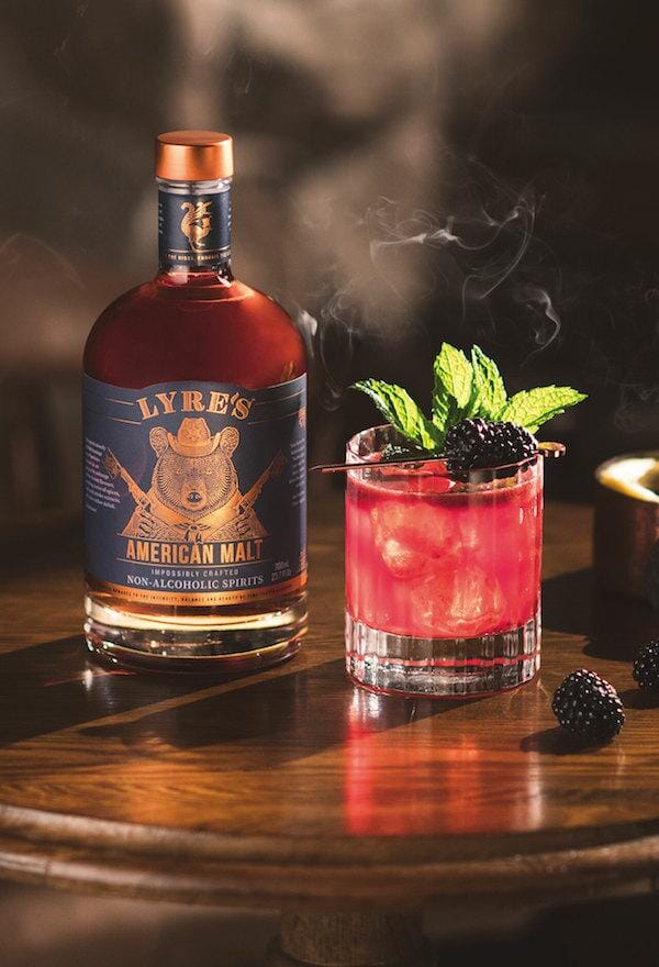 Blackberry Smash Whiskey Mocktail garnished with blackberries and mint leaves next to a bottle of Lyre's American Malt