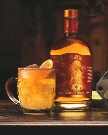 Dark and Spicy Rum Mocktail garnished with lime next to a bottle of Lyre's Spiced Cane Spirit