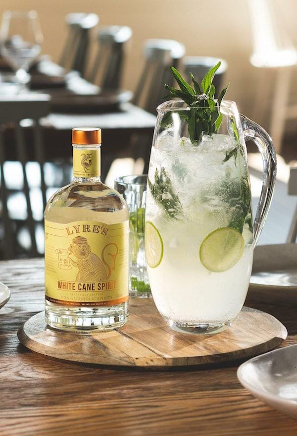 Bottle of Lyre’s White Cane Spirit next to a carafe of Mojito mocktails garnished with mint sprigs