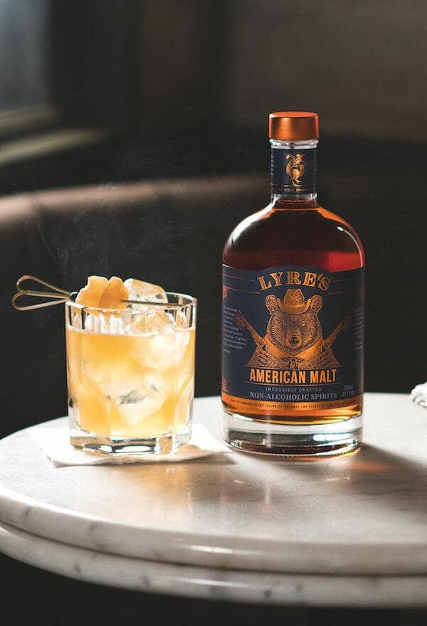 Bottle of Lyre's American Malt next to a whiskey mocktail garnished with a ginger skewer