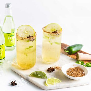 Two Spicy Margarita Mocktails garnished with apple slices in tall glasses rimmed with cinnamon Sans Drinks