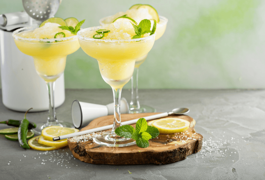 Three frozen non-alcoholic margarita mocktails garnished with lemon slices and mint Sans Drinks