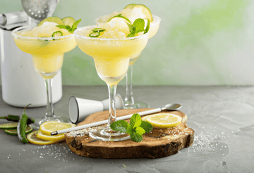 Three frozen non-alcoholic margarita mocktails garnished with lemon slices and mint Sans Drinks