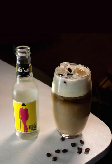 Coffee mocktail garnished with coffee beans next to a bottle of Artisan Drinks Classic London Tonic