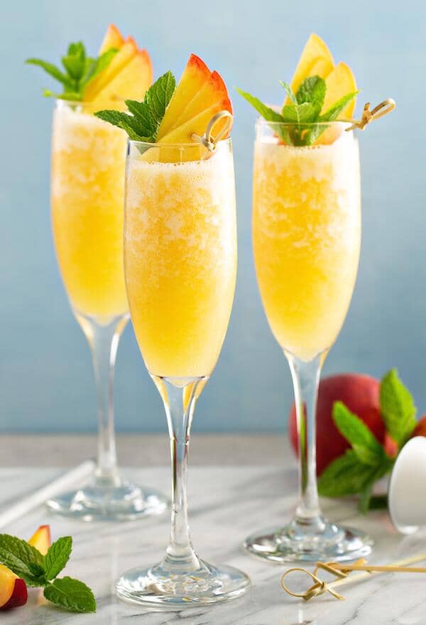 Three Non-alcoholic peach bellini in champagne glasses garnished with strawberries and mint leaves