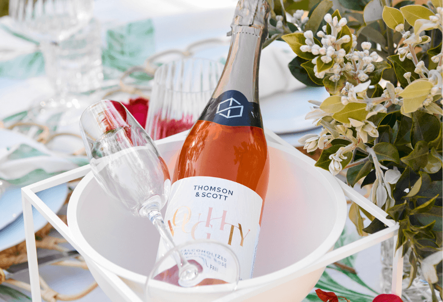 A bottle of Thomson & Scott Noughty Rose next to a champagne glass on a drinks cooler ice bucket