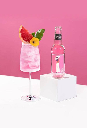 Bottle of Artisan Pink Citrus Tonic next to a glass of spritz mocktail garnished with edible flowers and a slice of grapefruit