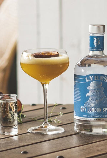 Tropical martini mocktail garnished with passionfruit shell in a coupe glass next to a bottle of Lyre's Dry London Spirit