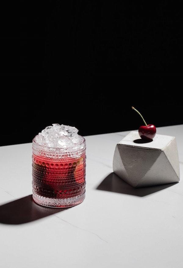 Cherry smash mocktail garnished with lime wedges in a glass filled with crushed ice Sans Drinks