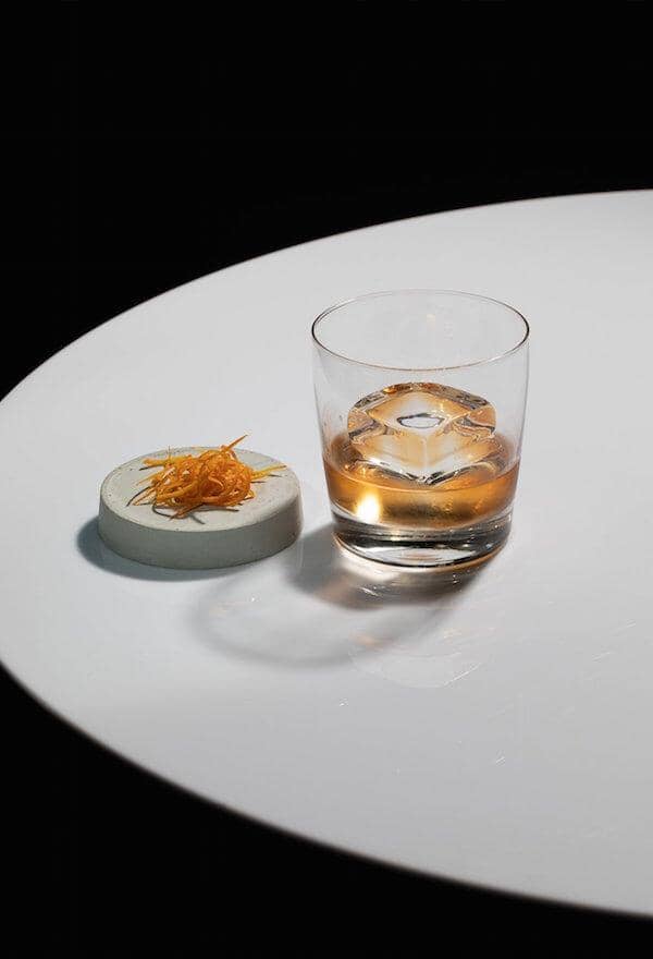 Old Fashioned Rum Mocktail in a rock glass with a clear ice block Sans Drinks