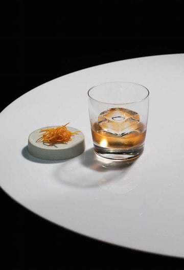 Old Fashioned Rum Mocktail in a rock glass with a clear ice block Sans Drinks