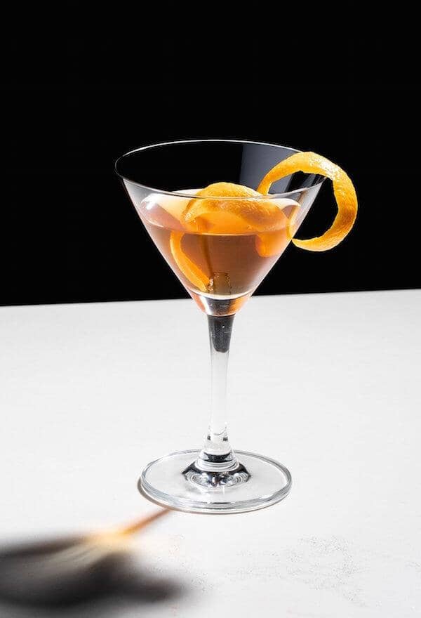 Rum mocktail in a martini glass garished with orange zest Sans Drinks