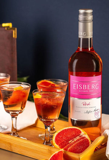 Three glasses of Rosé and Grapefruit Spritz garnished with blood orange slices next to a bottle of Eisberg Alcohol-Free Rosé