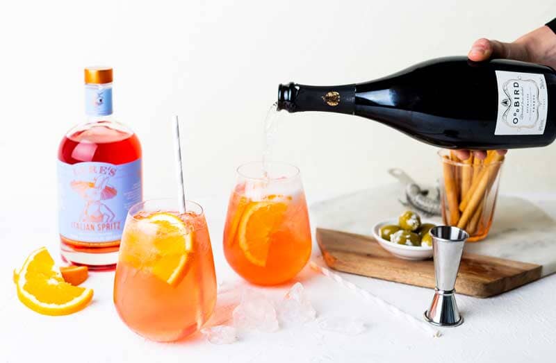 A bottle of Odd Bird non-alcoholic prosecco being poured into a glass filled with Lyre's italian spritz