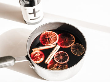 Non-alcoholic mulled wine in a pot with cinnamon sticks and orange slices next to a bottle of Plus and Minus Pinot Noir