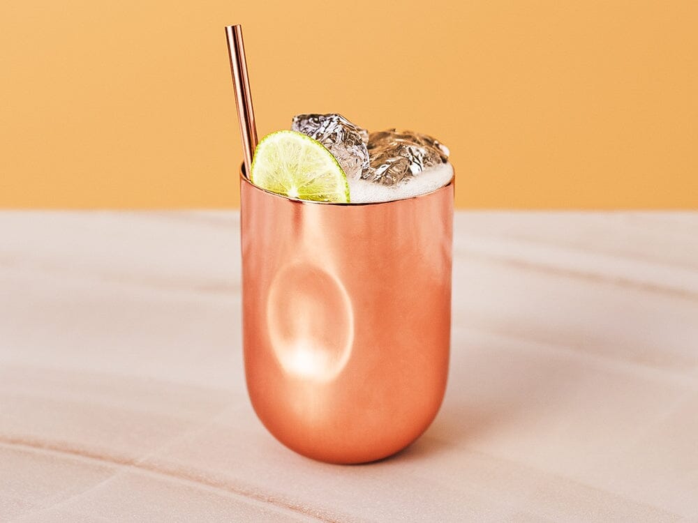 Light gin mocktail in a copper cup garnished with lime slice Sans Drinks