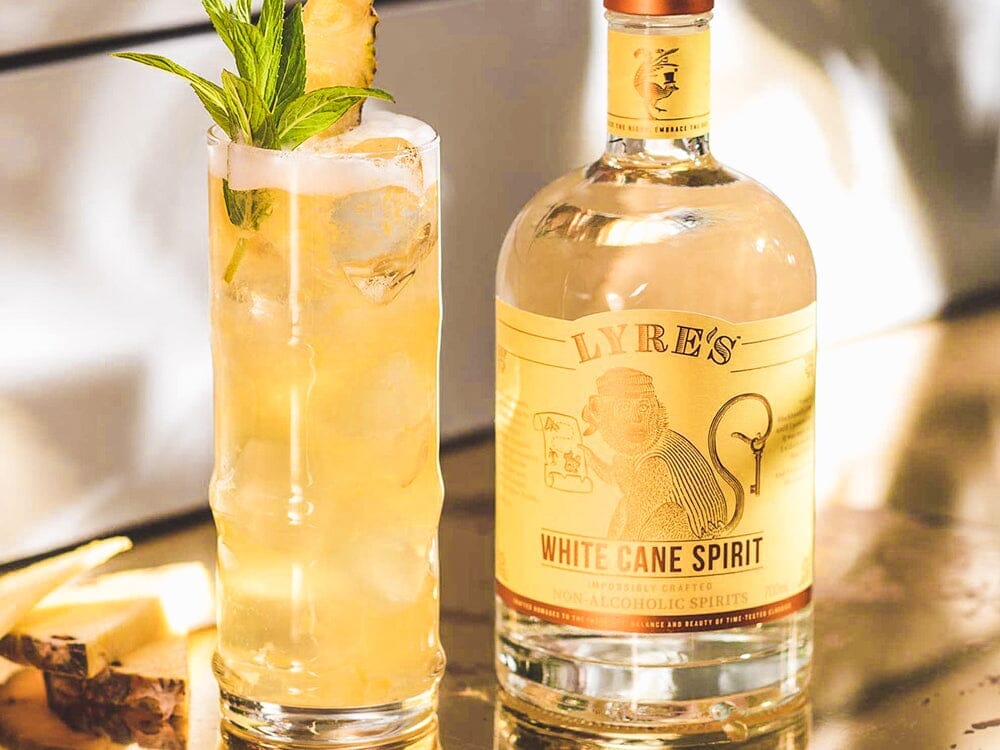 Bottle of Lyre's White Cane Spirit next to a glass of Pina Colada mocktail Sans Drinks