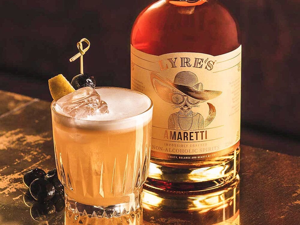 Sour Mocktail garnished with a slice of lemon next to a bottle of Lyre's Amaretti 