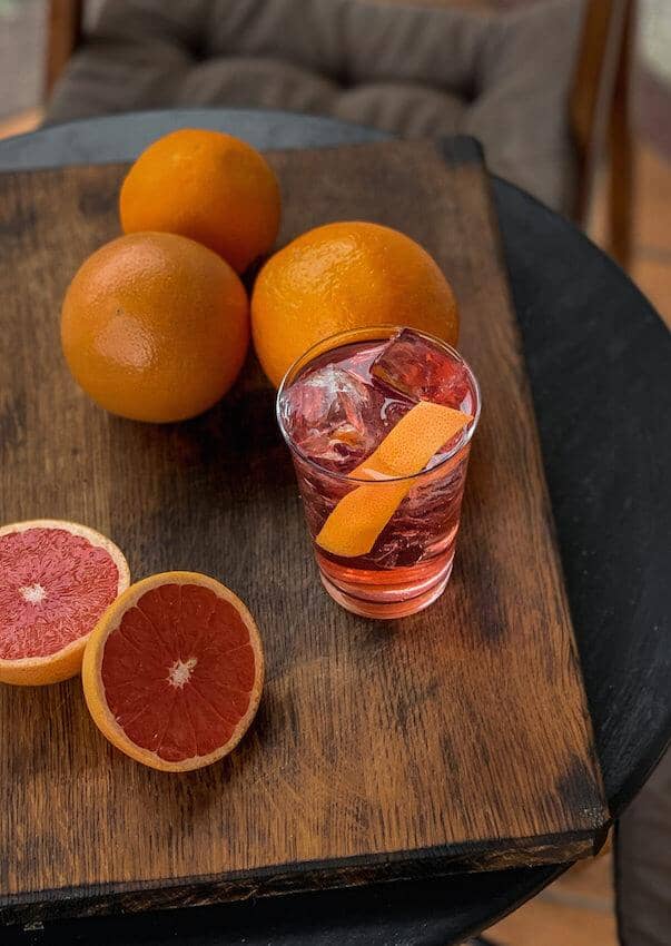 Pink gin mocktail garnished with an orange slice on a table filled with oranges