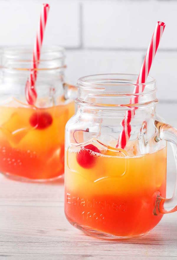 Two jars of non-alcoholic Tequila Sunrise made with Ms Sans Bring a Sombrero Non-alcoholic tequila and garnished with cherries