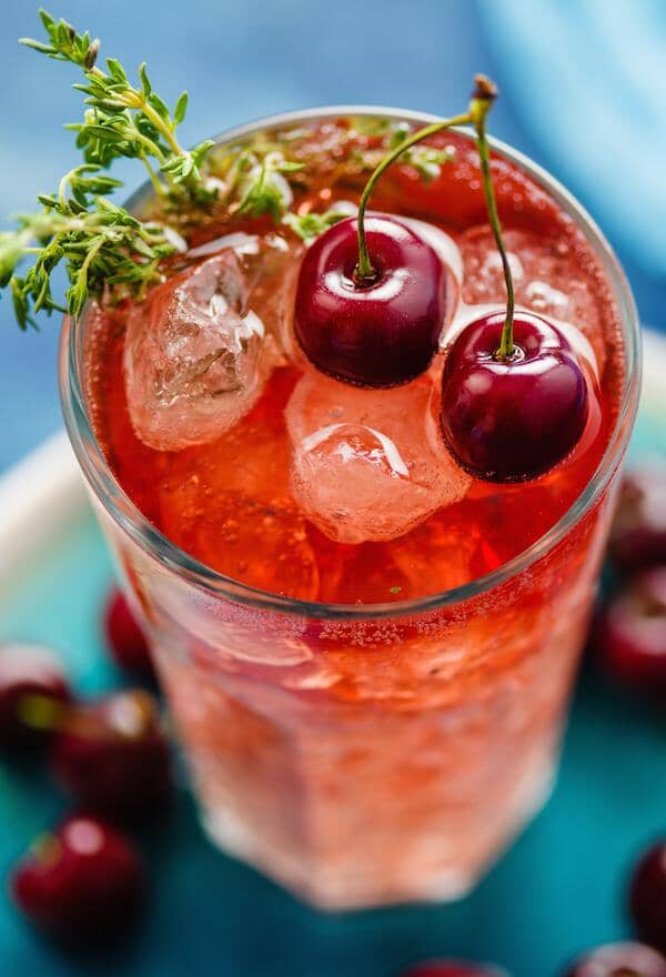 Singer Champagne Mocktail in a glass filled with ice and garnished with fresh cherries