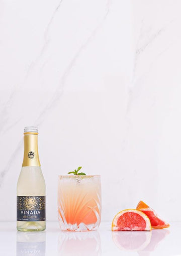 Bottle of VINADA Crispy Chardonnay next to a grapefruit sparkle champagne mocktail