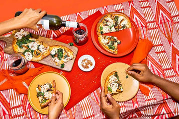 A table with pizza and a women pouring non-alcoholic wine into a glass Sans Drinks