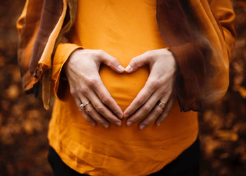Pregnant woman holding her belly with heart hands