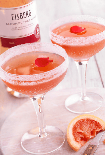 Two glasses of Rosé Mocktail garnished with rose petals next to a bottle of Eisberg's alcohol-free rosé