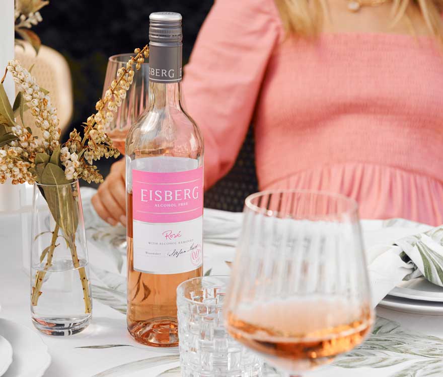 A bottle of Eisberg Non-alcoholic Rose on a dinner table next to a glass filled with non-alcoholic rose