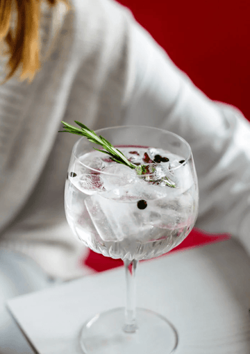 Woman with a gin and tonic mocktail garnished with berries and fresh rosemary