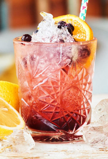 Pink Gin Bramble garnished with brambles and lemon slices