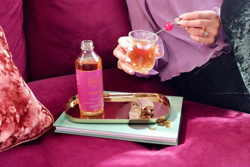 A bottle of Monday Distillery non-alcoholic spirit on a tray and a woman holding a mocktail